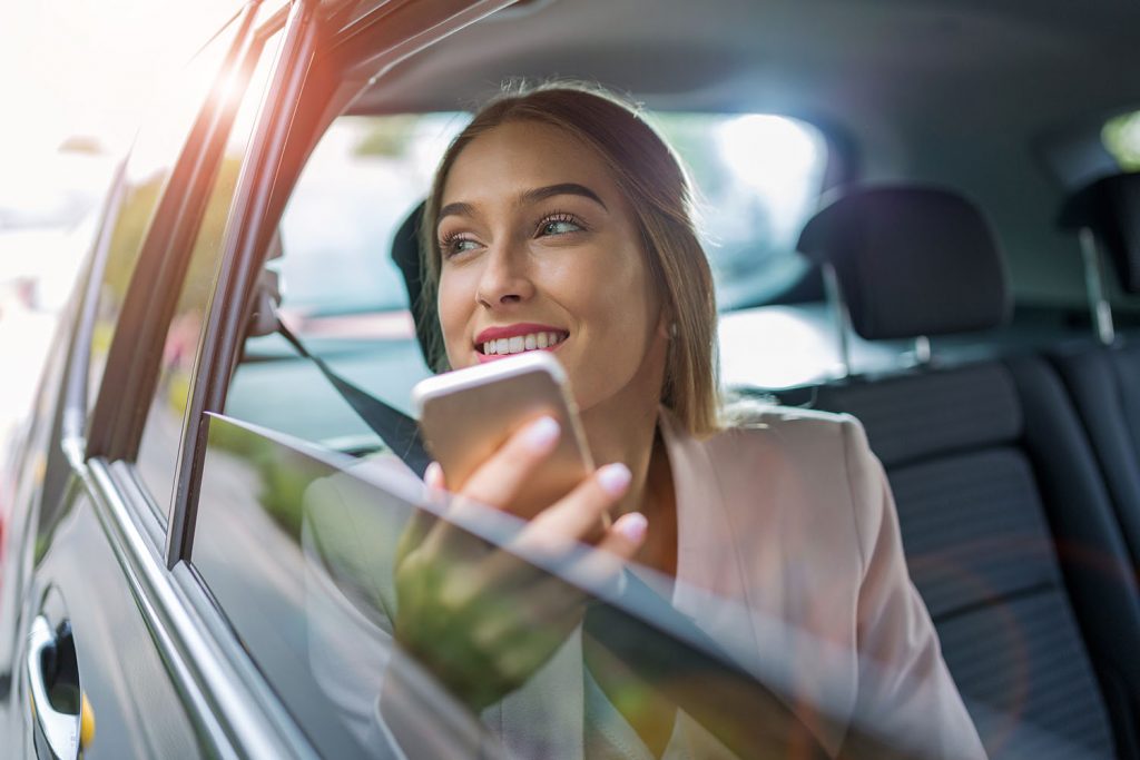 Frau mit Smartphone sieht auf der Rücksitzbank eines Autos aus dem Fenster
